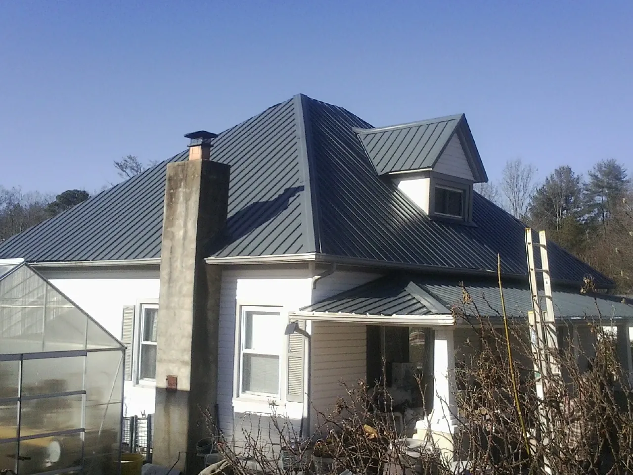 Dark blue standing seam metal roof on a white farmhouse with dormer — Slate & Tile Roof Repair by Roofing Brothers in Hotchkiss