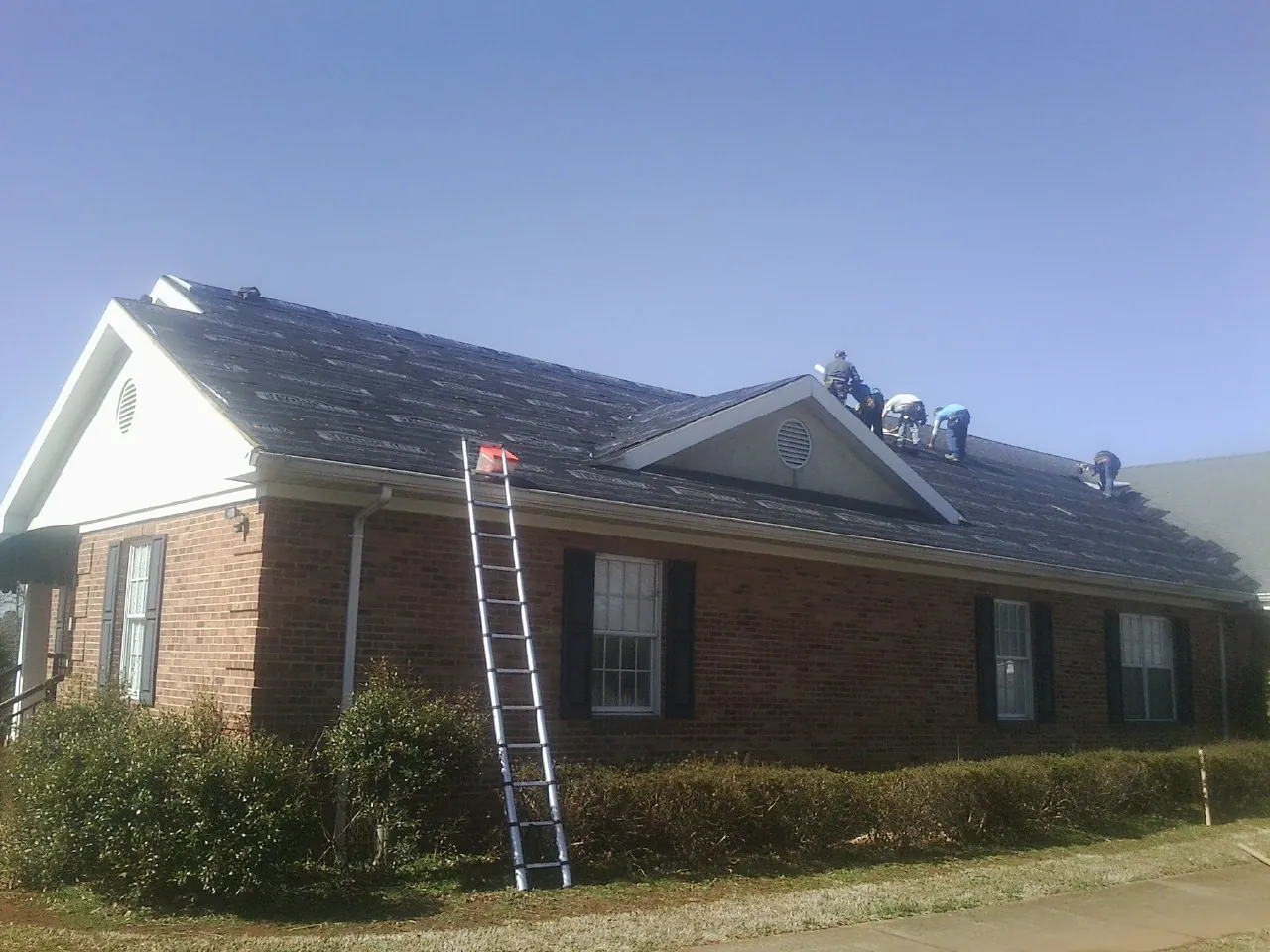 Crew tearing shingles off a brick ranch roof with a ladder set — Emergency Roof Repair work by our crew in Hotchkiss
