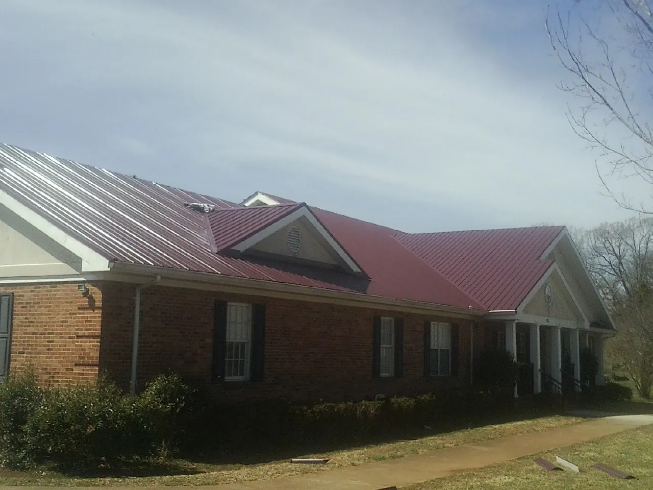 Red metal roof with gabled entries on a long brick building, from a Hail Damage Roof Repair job in Hotchkiss