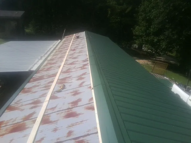Old rusted panels beside newly installed green metal roofing — Wind Damage Roof Repair by Roofing Brothers in Hotchkiss