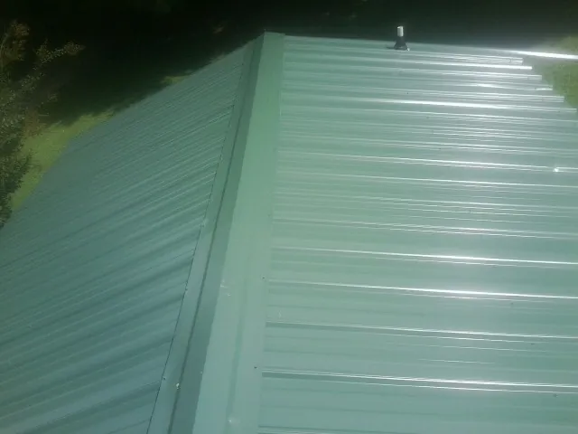 New green metal panels meeting at the ridge of a roof — Flat Roof Repair work by our crew in Hotchkiss