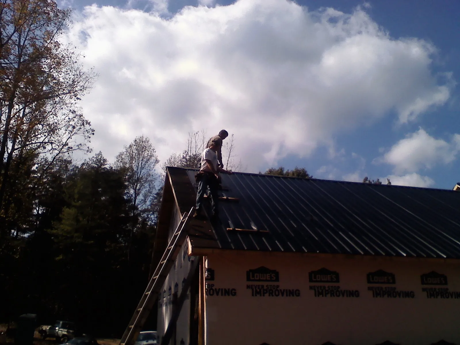 Roofer fastening dark metal panels high against a cloudy sky, from a Roof Inspection job in Hotchkiss