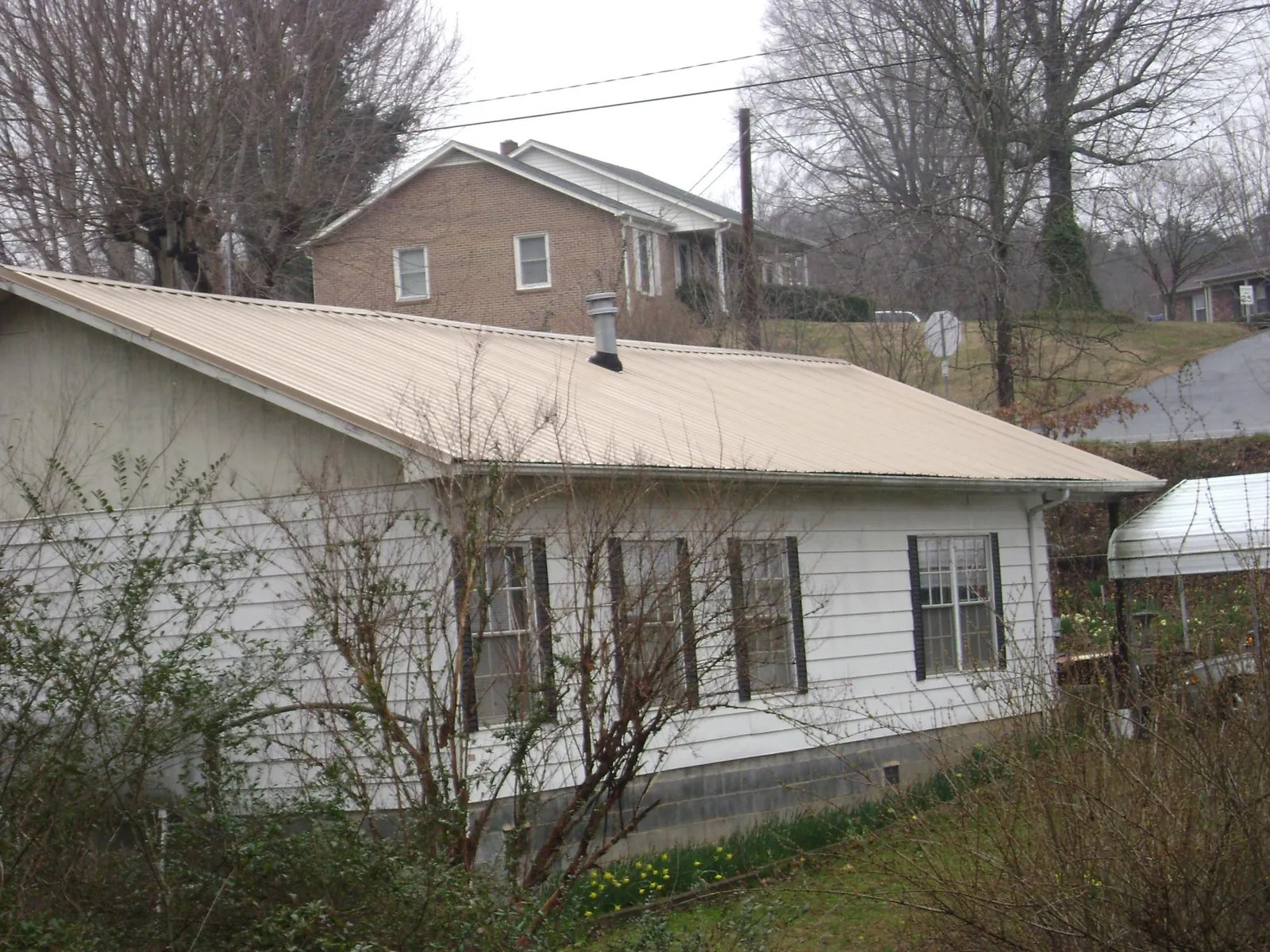 Tan metal roof on a white sided house set into a hillside — Commercial Roofing by Roofing Brothers in Hotchkiss