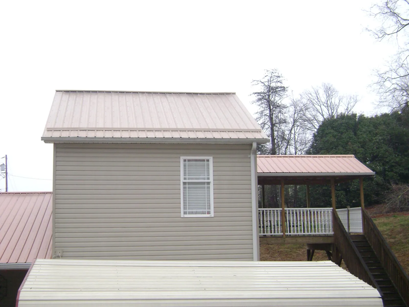 Tan metal roofs on a two story addition and attached porch, from a Roof Replacement job in Hotchkiss